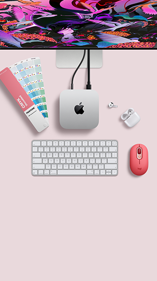 Un Mac mini visto dall’alto, alluminio color argento, angoli arrotondati, logo Apple nero lucido al centro, collegato via cavo a Studio Display parzialmente visibile in alto, AirPods 4 con custodia aperta, campioni di colore Pantone, tastiera e mouse